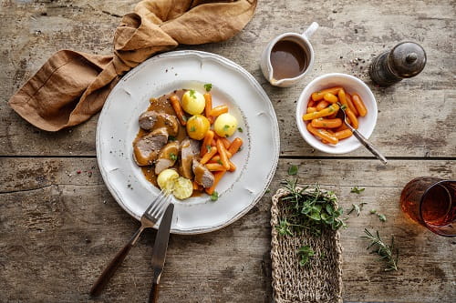 Entenbrust in brauner Soße mit kleinen Kartoffeln und Möhren auf rustikalem Holztisch