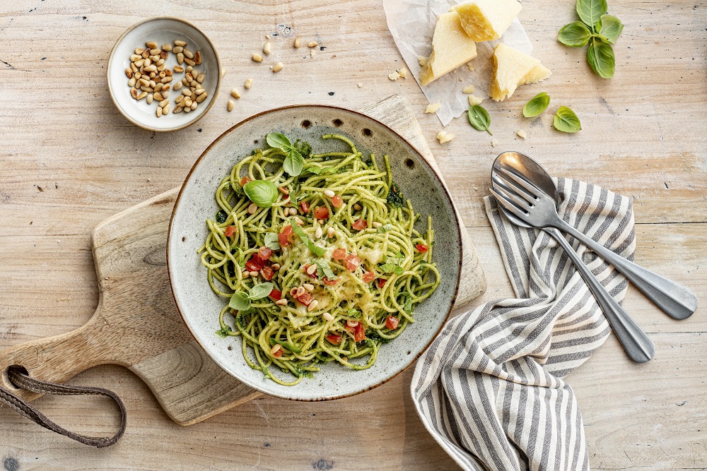 Spaghetti in Pesto, mit frischen Tomatenwürfeln, geriebenem Käse und Basilikum garniert