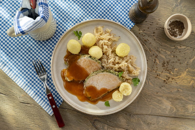 Ein hergerichteter Krustenbraten mit Beilage auf einer bayrischen Tischdecke