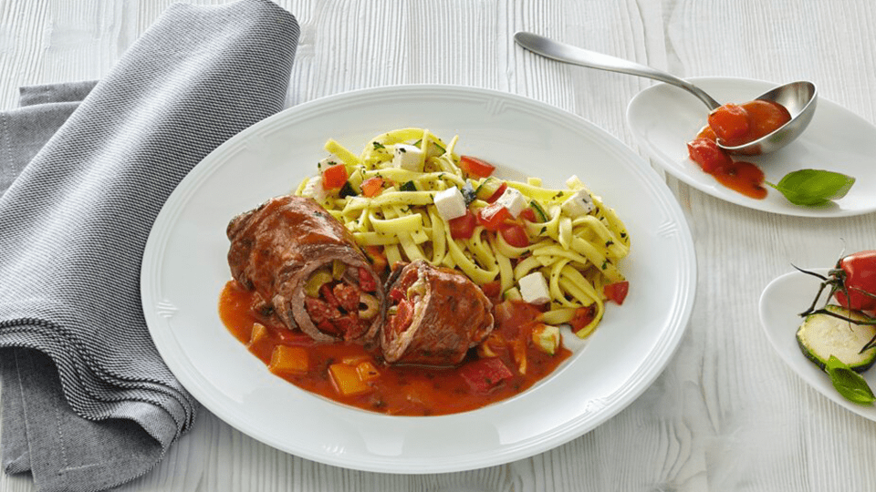 Gefüllte Rinderroulade in Tomatensoße, serviert mit Kräuterbandnudeln und Tomatenwürfeln