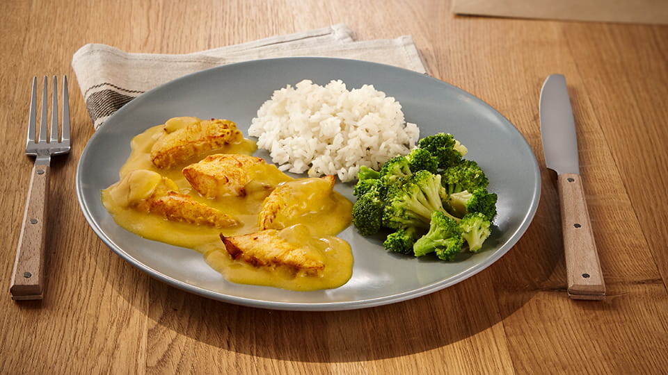 Hähnchenfiletstücke in gelber Currysoße, dazu Reis und Brokkoli