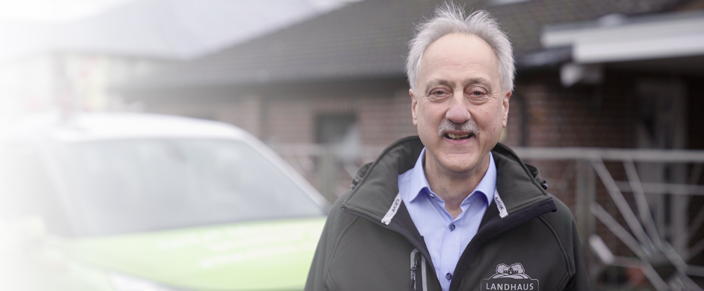 Älterer Mann lacht und trägt eine Jacke mit Logo der Landhausküche