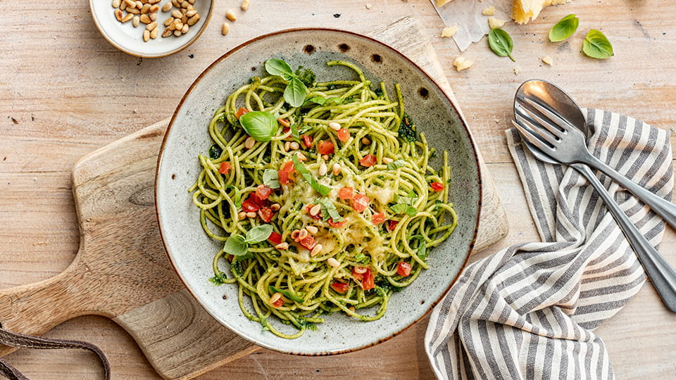 Spaghetti in Pesto, mit frischen Tomatenwürfeln, geriebenem Käse und Basilikum garniert