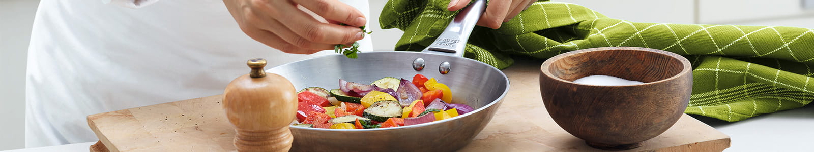 Köchin würzt ein Pfannengericht mit frischen Kräutern