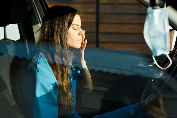 Frau in Arbeitskleidung der Pflege sitzt erschöpft im Auto
