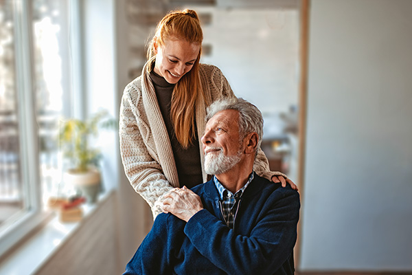 Junge Frau lacht einem sitzendem älteren Mann zu