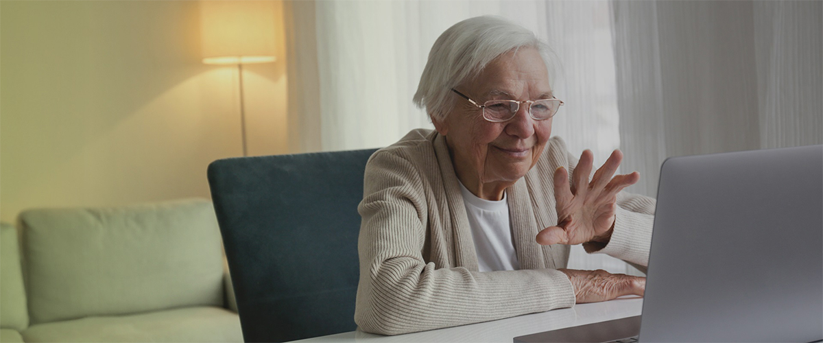 Ältere Frau sitzt am Tisch und lächelt in einen Laptop