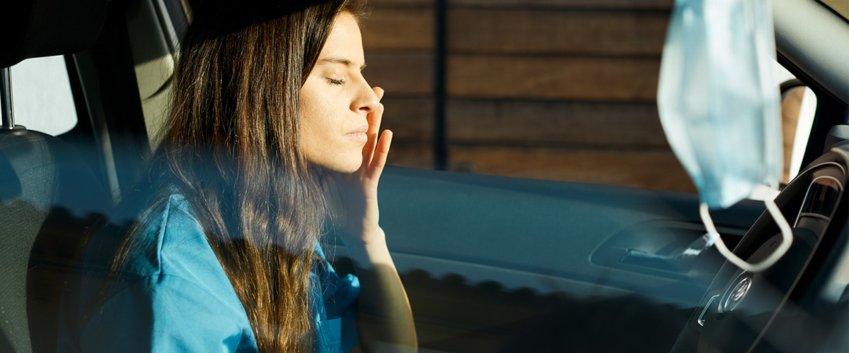 Pflegekraft sitzt erschöpft im Auto