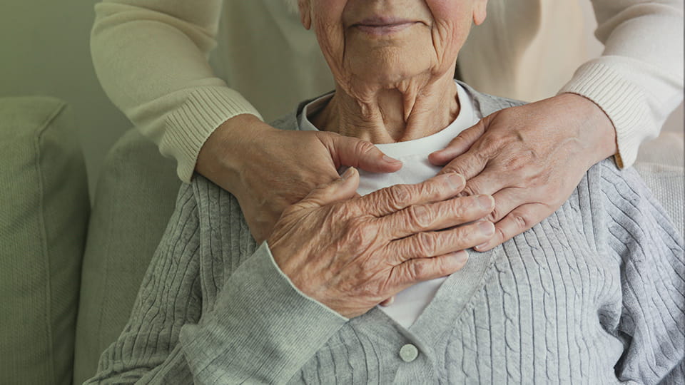 Seniorin hält die Hände einer anderen Person und lächelt dabei