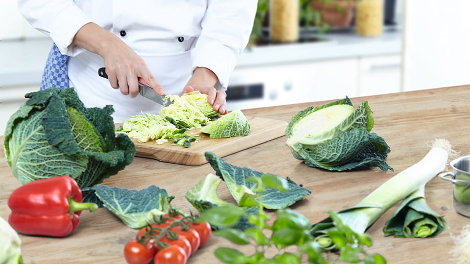 Koch in weißer Kleidung schneidet Salat auf einem Holzbrett