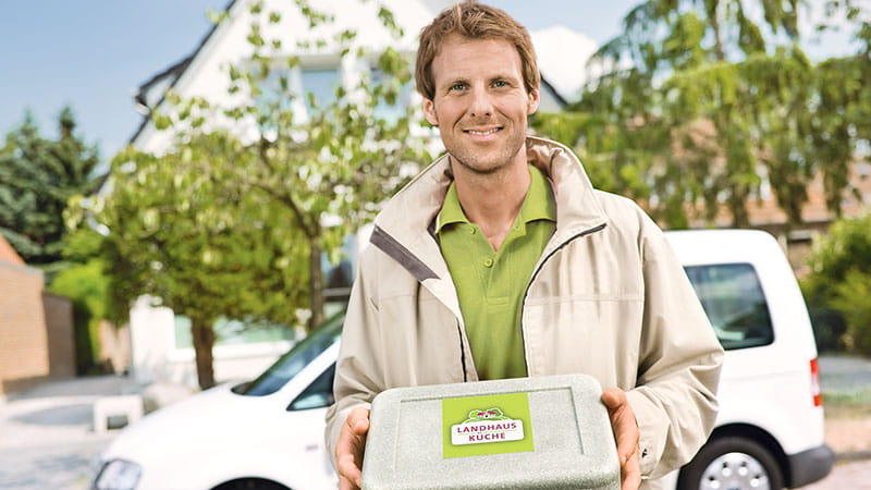 Lächelnder Kurier mit Landhausküche-Isolierbox vor einem weißen Lieferwagen
