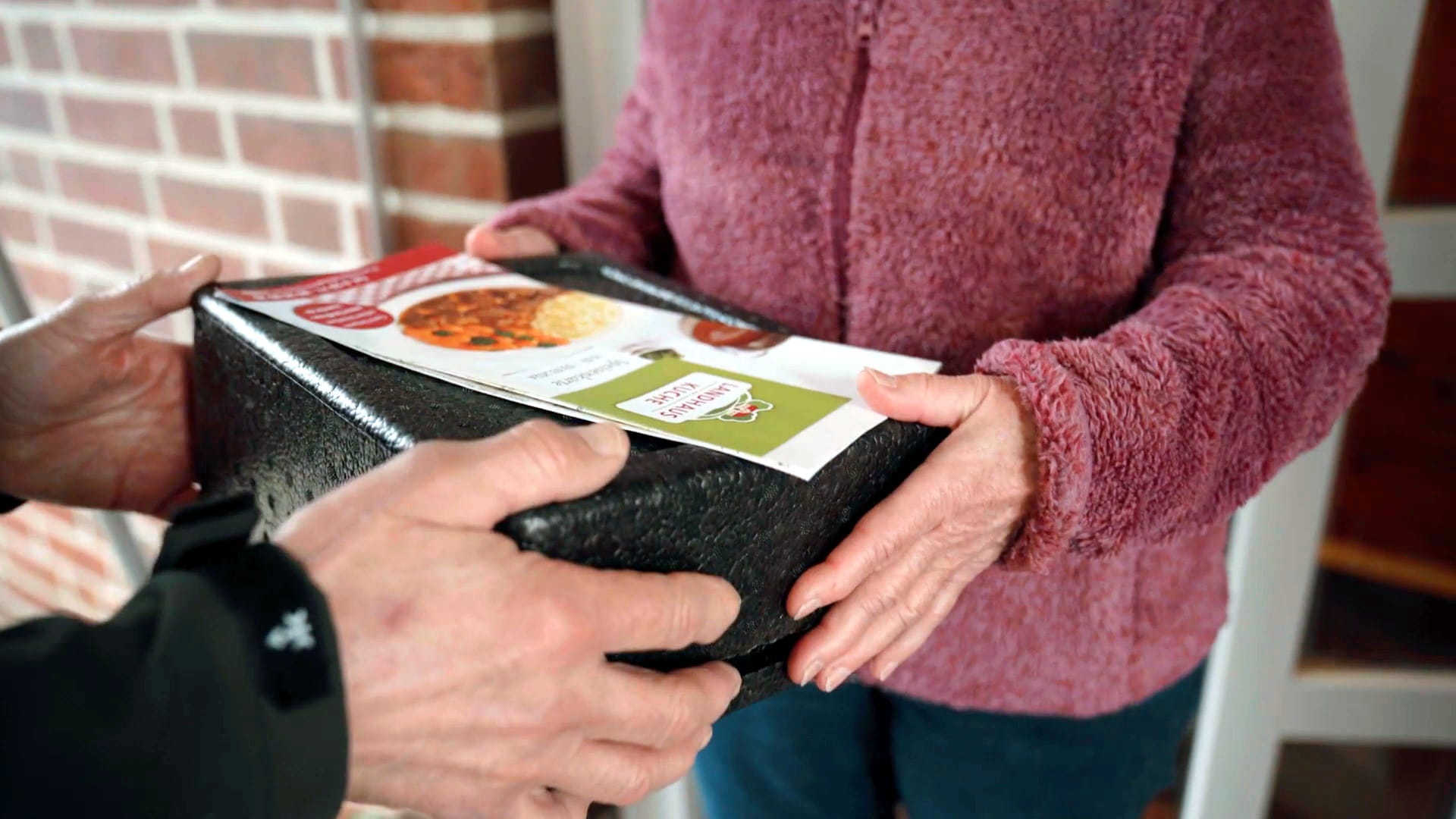 Mann übergibt Isolierbox an ältere Dame an der Haustür