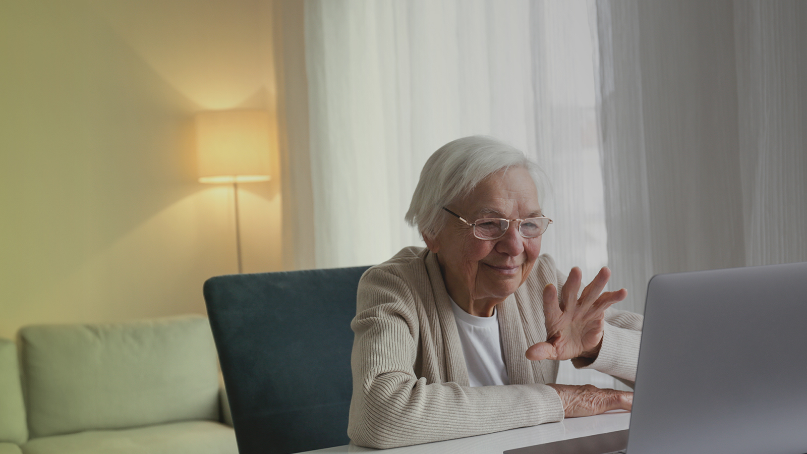 Ältere Frau sitzt am Tisch und lächelt in einen Laptop