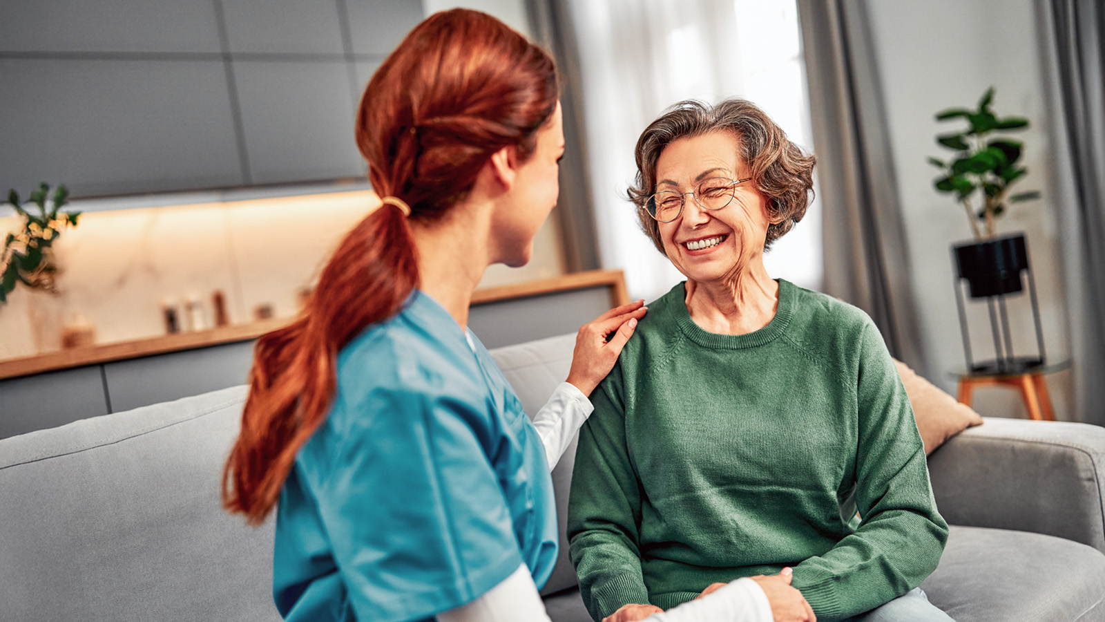 Pflegerin hält die Hand einer älteren Dame die lacht