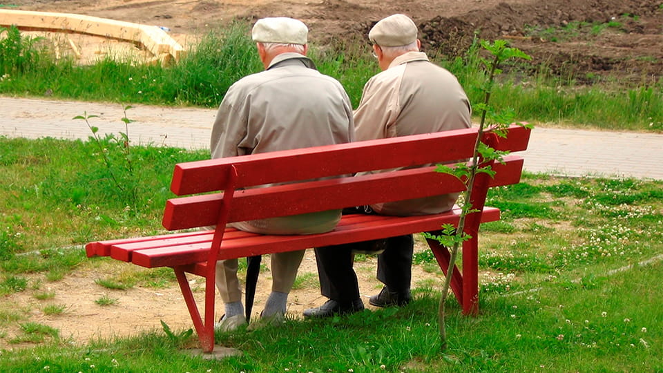 Zwei Senioren sitzen zusammen auf einer Bank und schauen in die Ferne