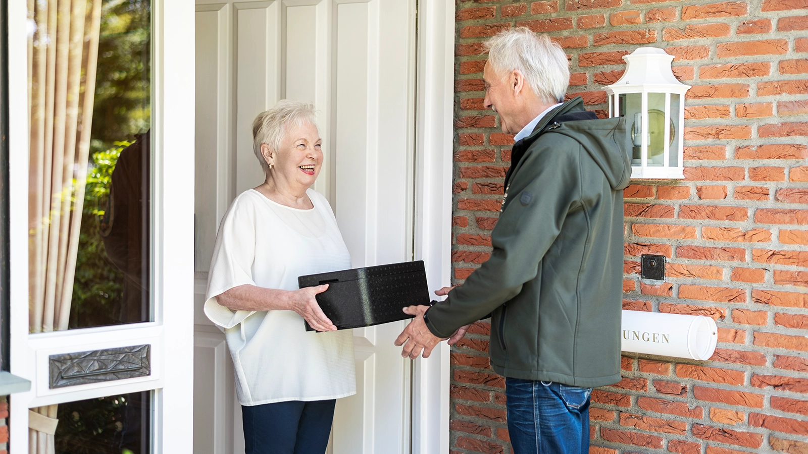 Ein Menükurier gibt einer Seniorin an ihrer Haustür ein Menü.