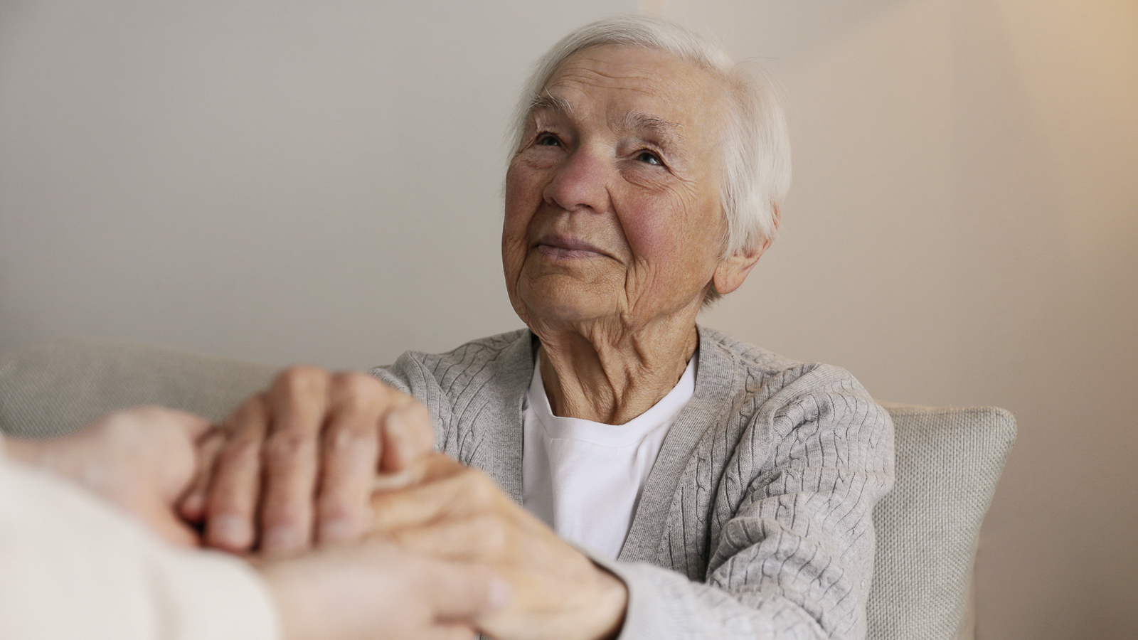 Seniorin hält die Hände einer anderen Person und lächelt dabei
