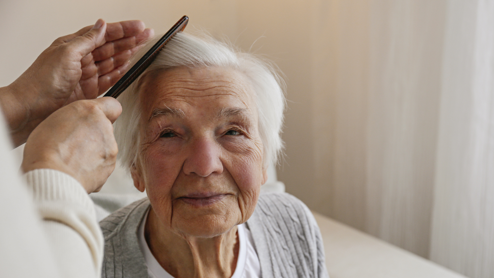 Einer älteren, lächelnden Frau werden die Haare gekämmt.
