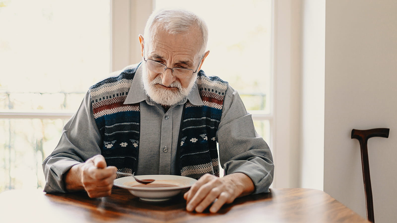 Älterer Mann sitzt am Tisch und isst eine Suppe