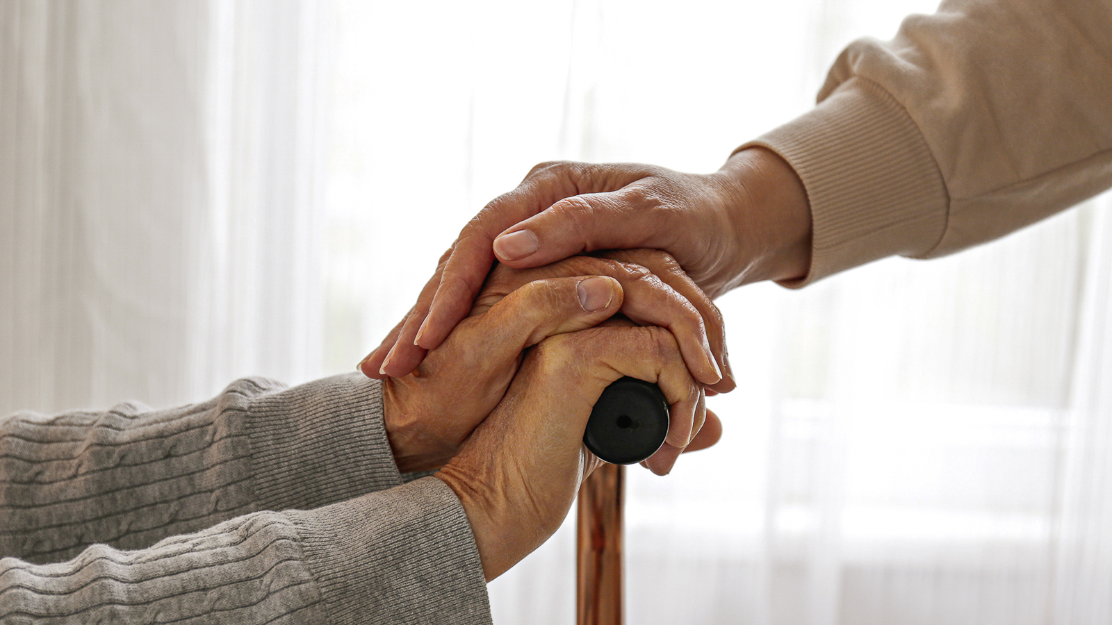 Ältere Frau hält Gehstock und wird durch eine Angehörige unterstützt.