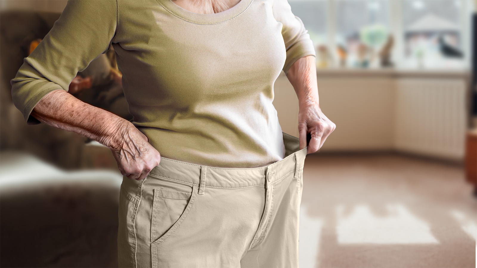 Eine ältere Frau hat an Gewicht verloren und probiert ihre zu weite Hose aus.