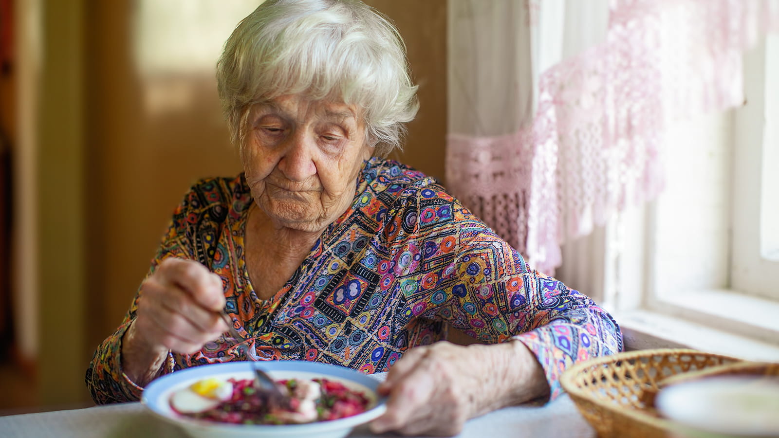 Eine ältere Frau sitzt alleine am Tisch und isst eine Suppe.