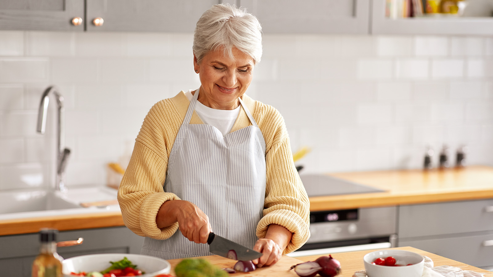 Eine ältere Frau schneidet in der Küche Gemüse auf einem Holzbrett