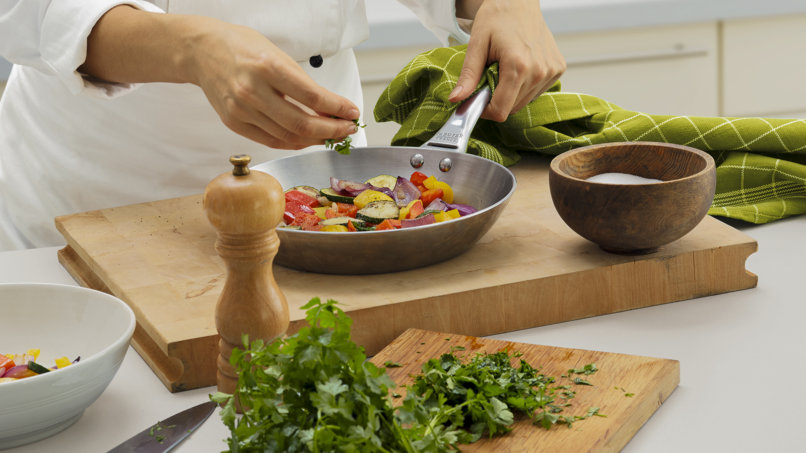 Eine Köchin würzt mit frischen Kräutern das Gemüse in einer Pfanne