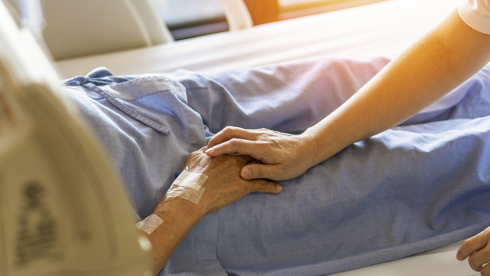 Ein Pfleger hält einer älteren Patientin die Hand am Krankenhausbett.