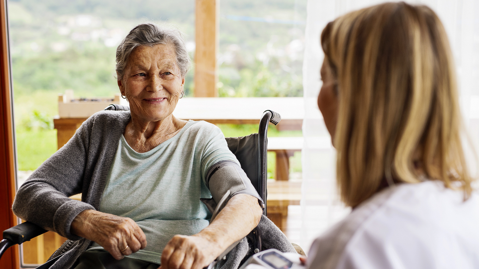 Seniorin sitzt beim Blutdruck messen im Rollstuhl.