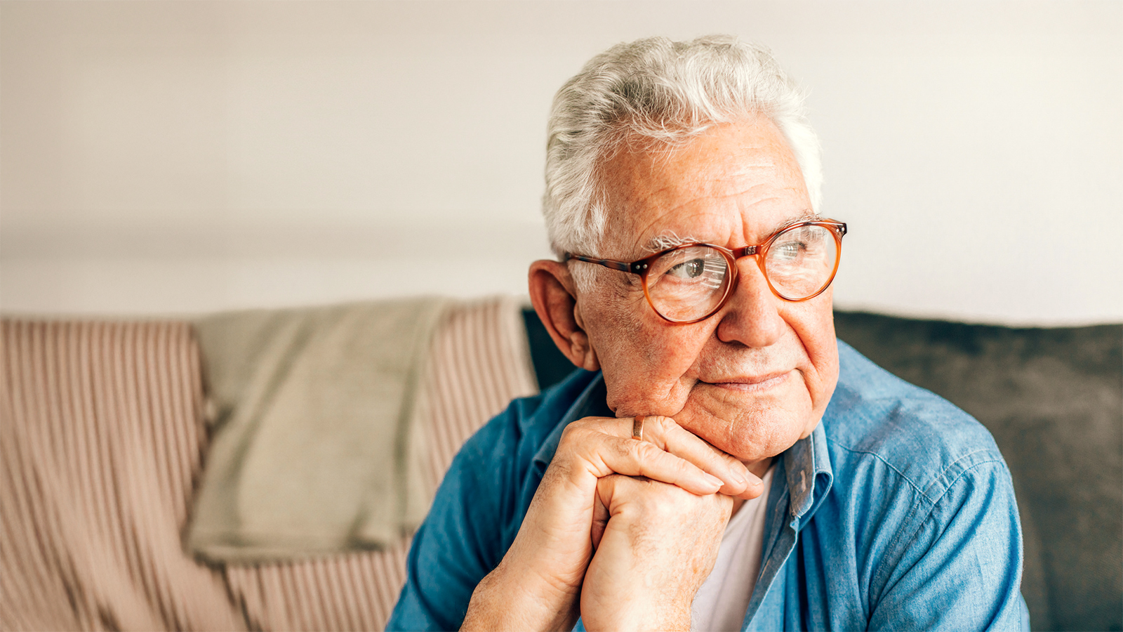Ein älterer Herr sitzt nachdenklich auf dem Sofa.