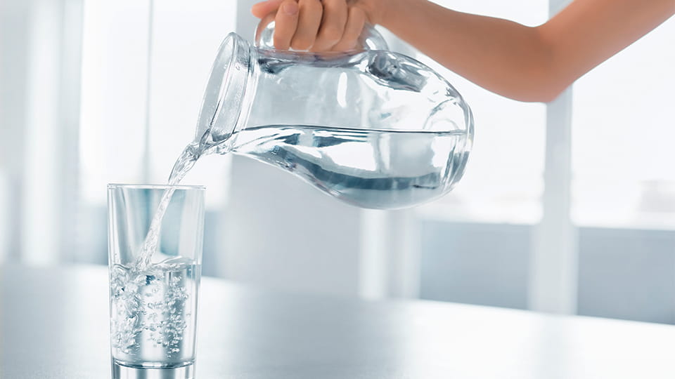 Person gießt Wasser aus Karaffe in ein Glas