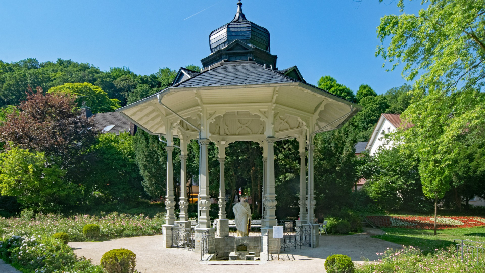 Weißer Pavillon mit Brunnen im Kurpark von Bad Soden, umgeben von Bäumen und Pflanzen