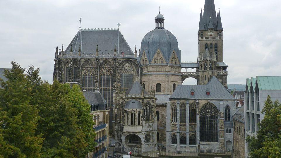 Blick auf den Aachener Dom, umgeben von Bäumen und Gebäuden.