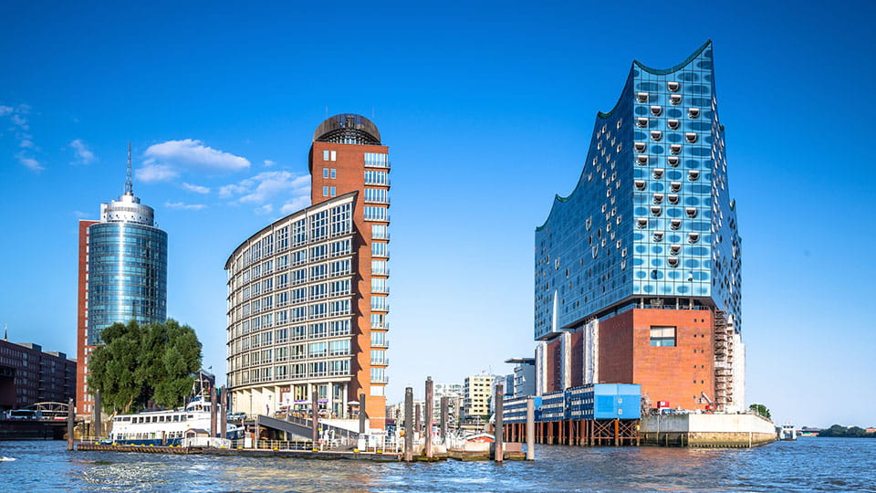 Hamburger Skyline mit der Elbphilharmonie und weiteren modernen Gebäuden am Ufer der Elbe bei blauem Himmel