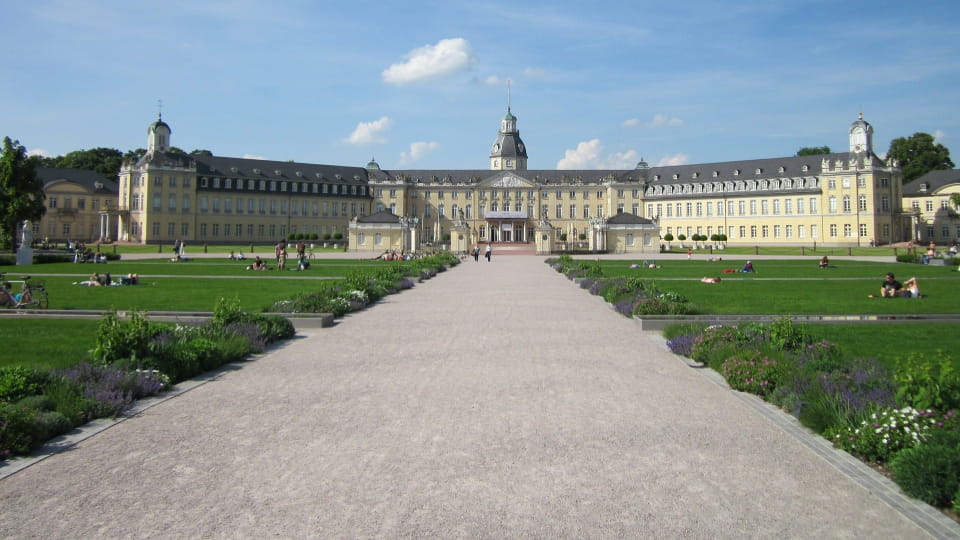 Blick auf das Karlsruher Schloss mit weitläufigem Vorplatz und Park, bei blauem Himmel