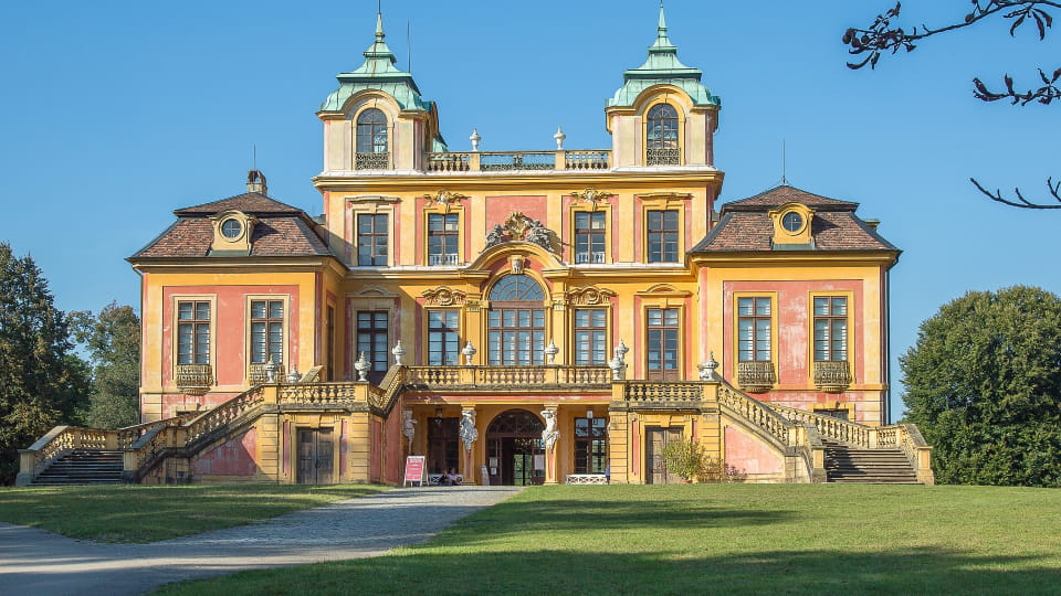 Das Schloss Favorite in Ludwigsburg mit hellgelber Fassade, grünen Kuppeln und breiter Treppe vor blauem Himmel