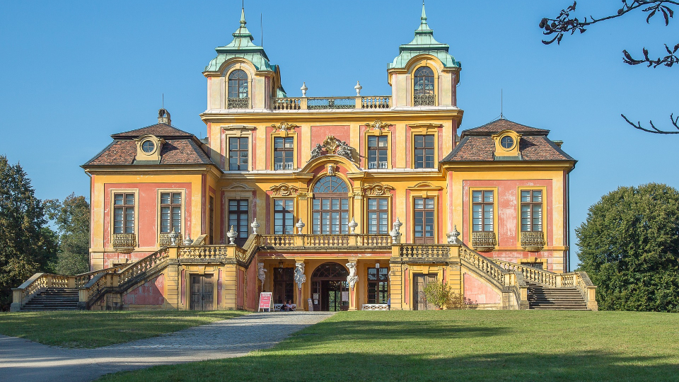 Das Schloss Favorite in Ludwigsburg mit hellgelber Fassade, grünen Kuppeln und breiter Treppe vor blauem Himmel