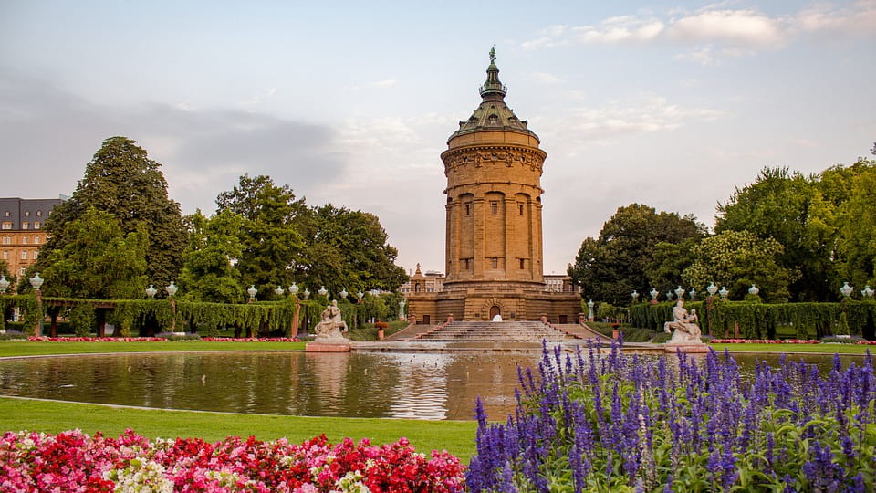 Wasserturm in Mannheim vor einem Springbrunnen, umgeben von Blumenbeeten und Bäumen