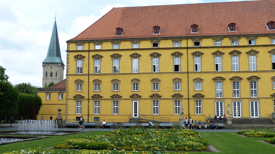 Gelbes barockes Schloss von Osnabrück mit rotem Dach, davor Springbrunnen und Blumenbeete