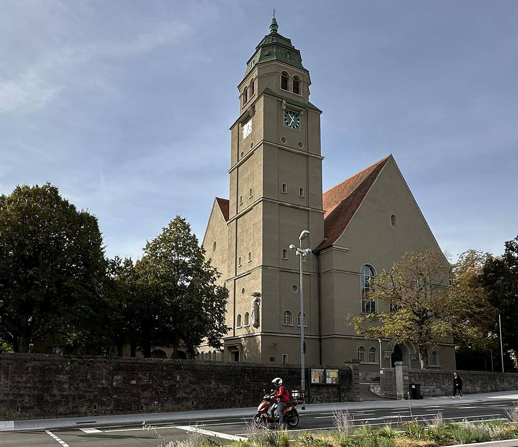 Christuskirche in Pforzheim mit großem Turm und Uhr und rotem Dach, umgeben von Bäumen und einer niedrigen Steinmauer