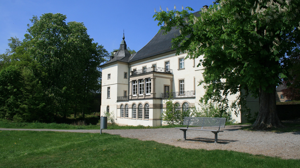 Helles Herrenhaus mit Garten, Parkbank und großen Bäumen