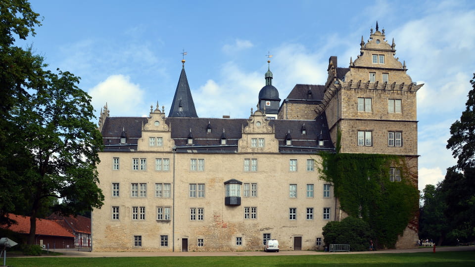 Historisches Schloss in Wolfsburg mit Türmen, umgeben von Bäumen und Rasenfläche