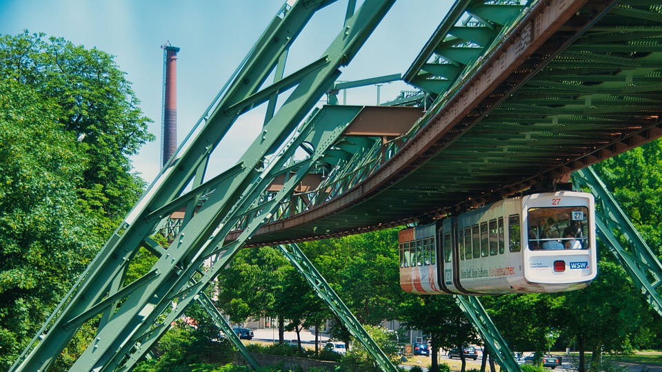 Schwebebahn in Wuppertal fährt unter grüner Stahlkonstruktion durch eine Stadt